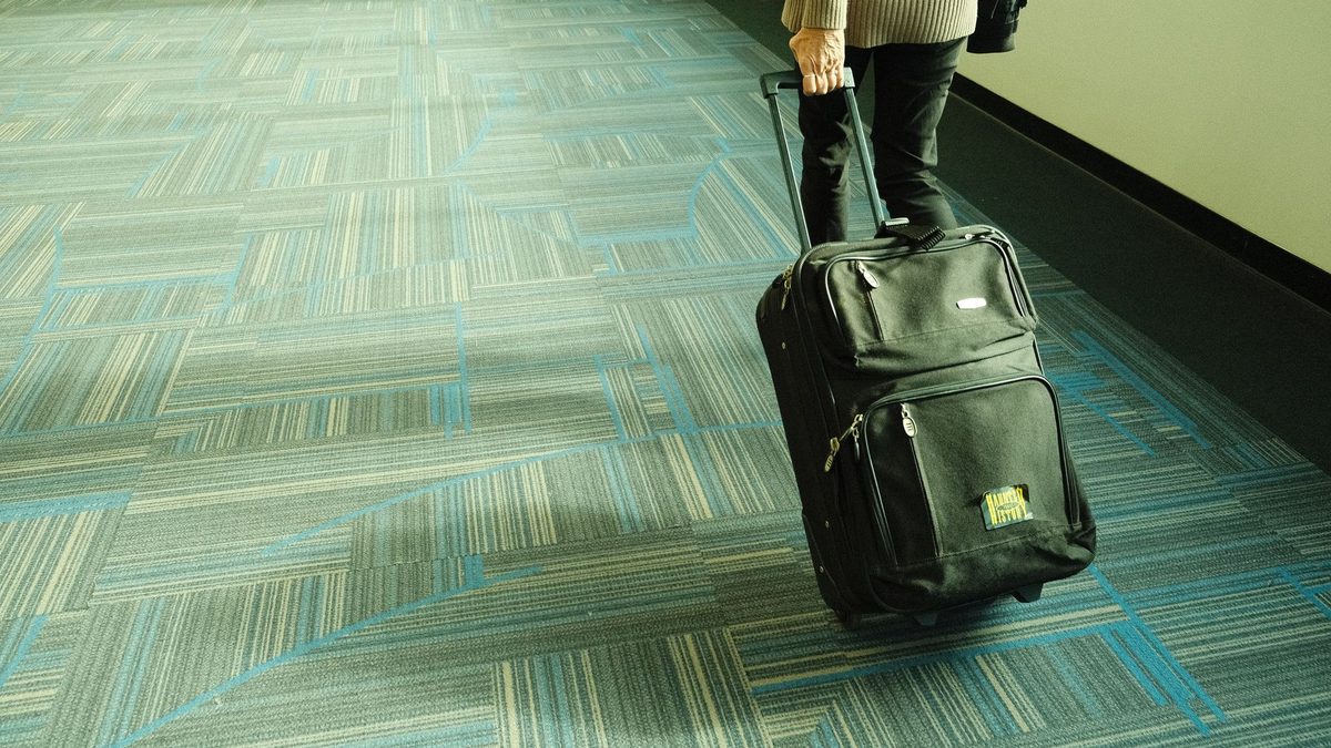공항 복도 카펫 위로 캐리어를 끌고 이동하는 여행자